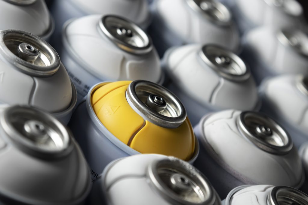 Zbliżenie na puszki aerozolu, jedna z nich wyróżniona żółtym elementem