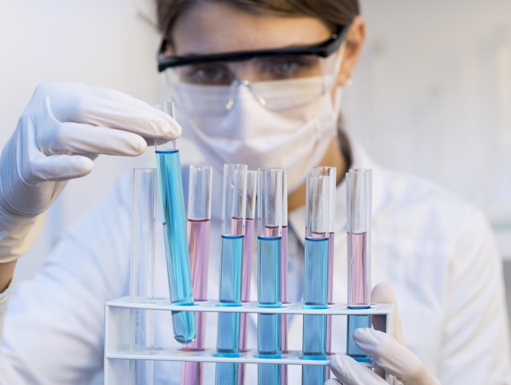 Pracownik laboratorium w rękawiczkach i maseczce analizuje próbki chemiczne w probówkach